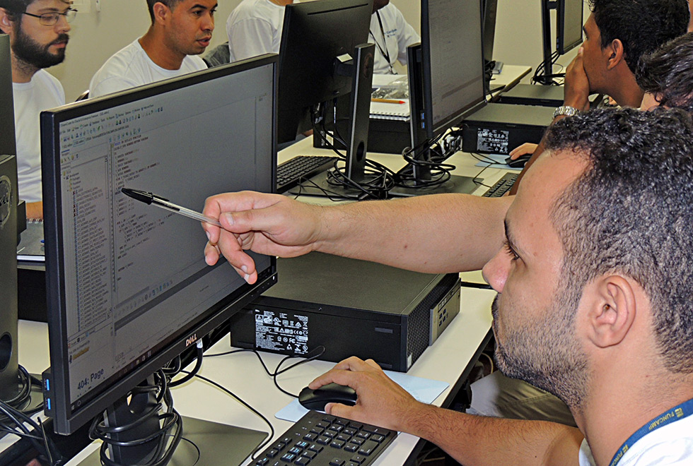Piloto e co-piloto tentam resolver os problemas Dupla de programadores em frente ao computador, um deles aponta para a tela