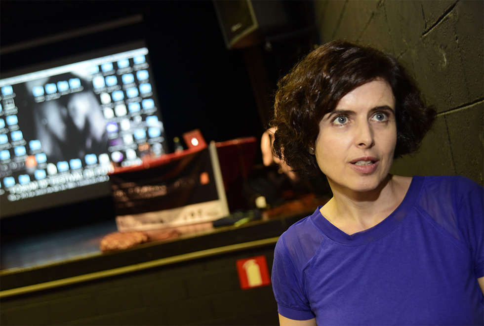 Ana Angélica Costa, curadora do eixo “Imagem Mágica” mulher em primeiro plano no canto direito da imagem. Ao fundo telão exibe imagens