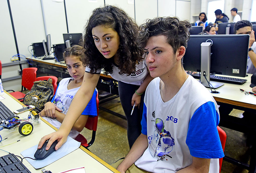 A monitora Luciana e os estudantes Maria Rita e João Pedro Luciana Dias ajuda Maria Rita e João Pedro na programação do robô