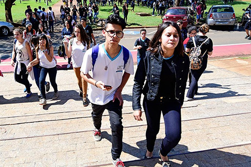 Audiodescrição: Em ampla área externa asfaltada, imagem de corpo inteiro e em perspectiva, uma grande fila com cerca de cinquenta jovens, formada da direita para a esquerda. Ao fundo na imagem, ha outros grupo de jovens. Imagem 1 de 1. Audiodescrição: Em ampla área externa asfaltada, imagem de corpo inteiro e em perspectiva, uma grande fila com cerca de cinquenta jovens, formada da direita para a esquerda. Ao fundo na imagem, ha outros grupo de jovens. Imagem 1 de 1.