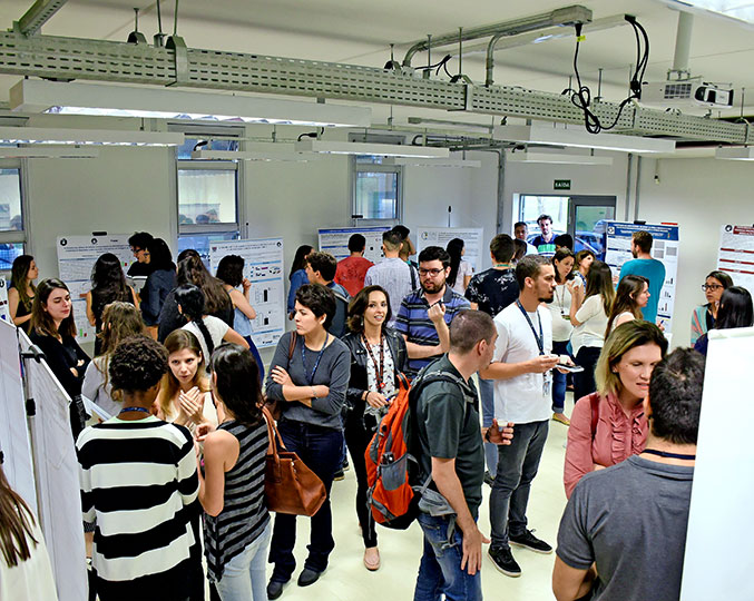 Apresentação de pôsteres de pesquisas desenvolvidas pelo OCRC imagem mostra várias pessoas em pé no espaço onde foi montada a exposição de pôsteres das pesquisas