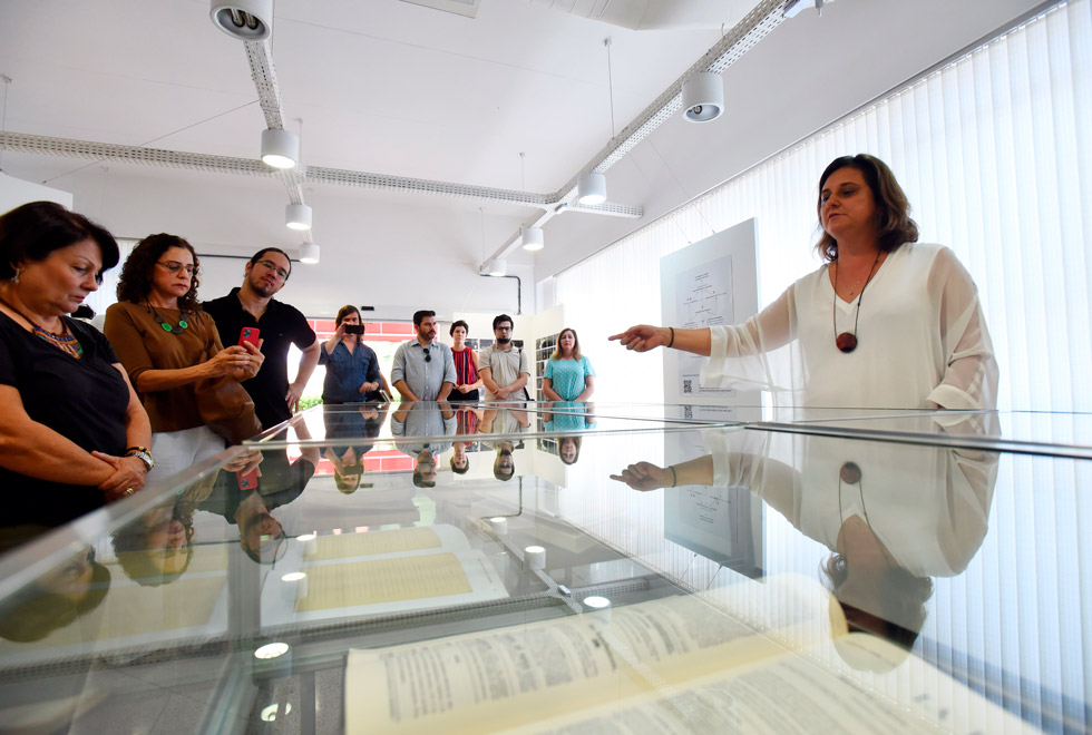 audescrição: A curadora Fabiana Bruno explica a visitantes como foi organizada a expoisção a 
