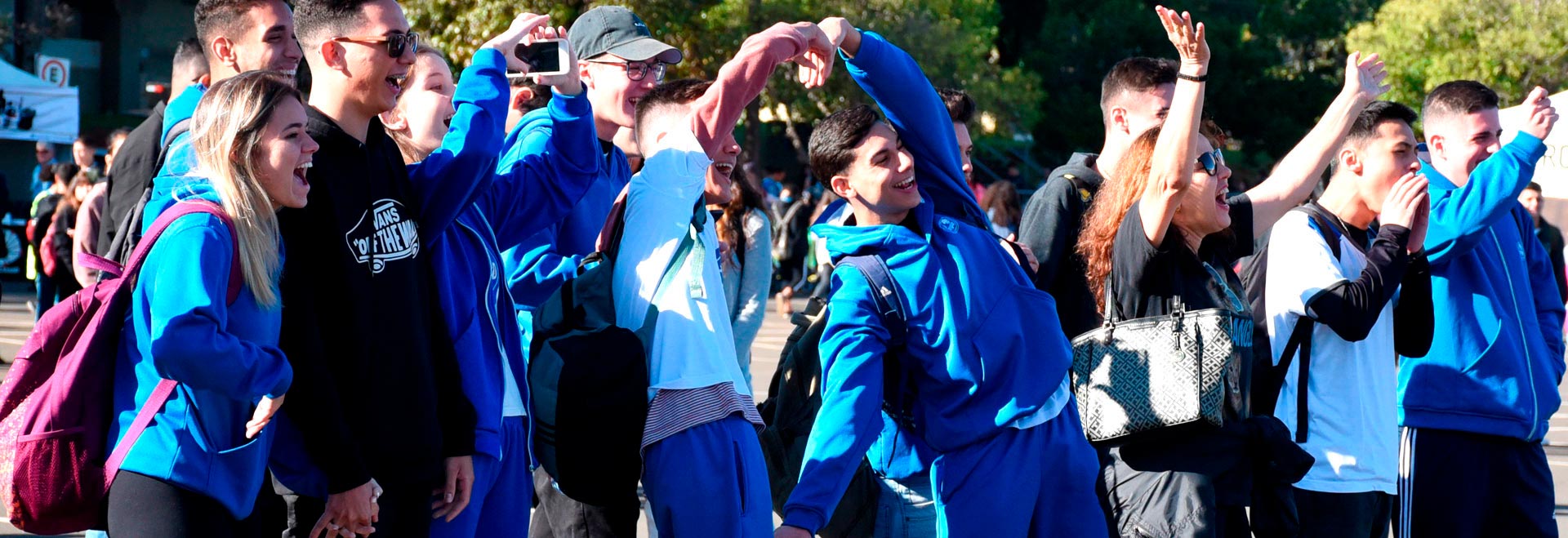 foto mostra alunos vestindo uniformes azuis fazendo brincadeiras para uma câmera
