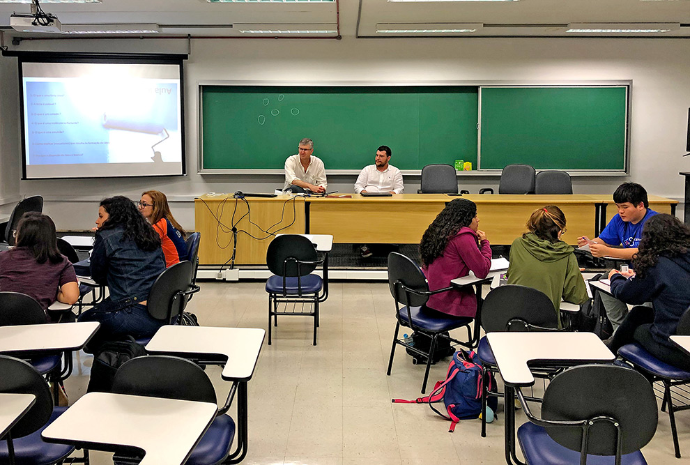 audiodescrição: fotografia colorida de sala de aula. na frente estão o professor edvaldo e o químico diego, ministrando aula. de costas, alguns alunos sentados nas carteiras de sala.