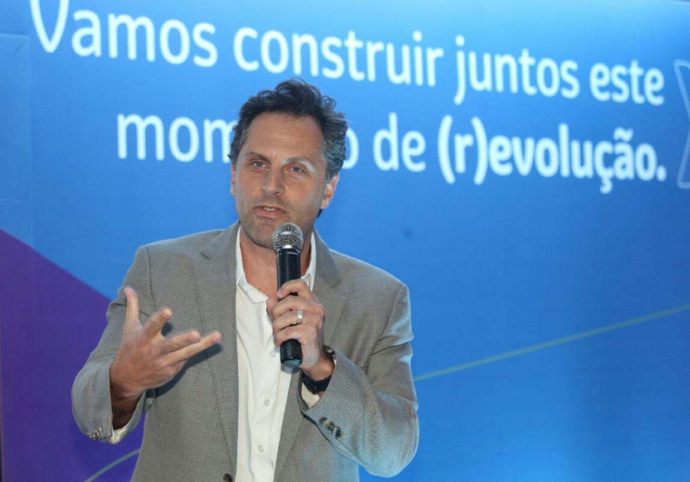 foto mostra daniel castanho em pé, com microfone em mãos, falando em um evento