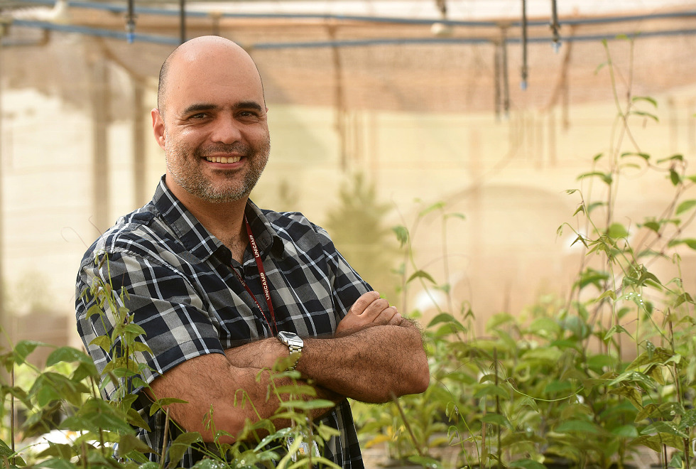 Professor Rafael de braços cruzados sorri para a foto em meio a plantas