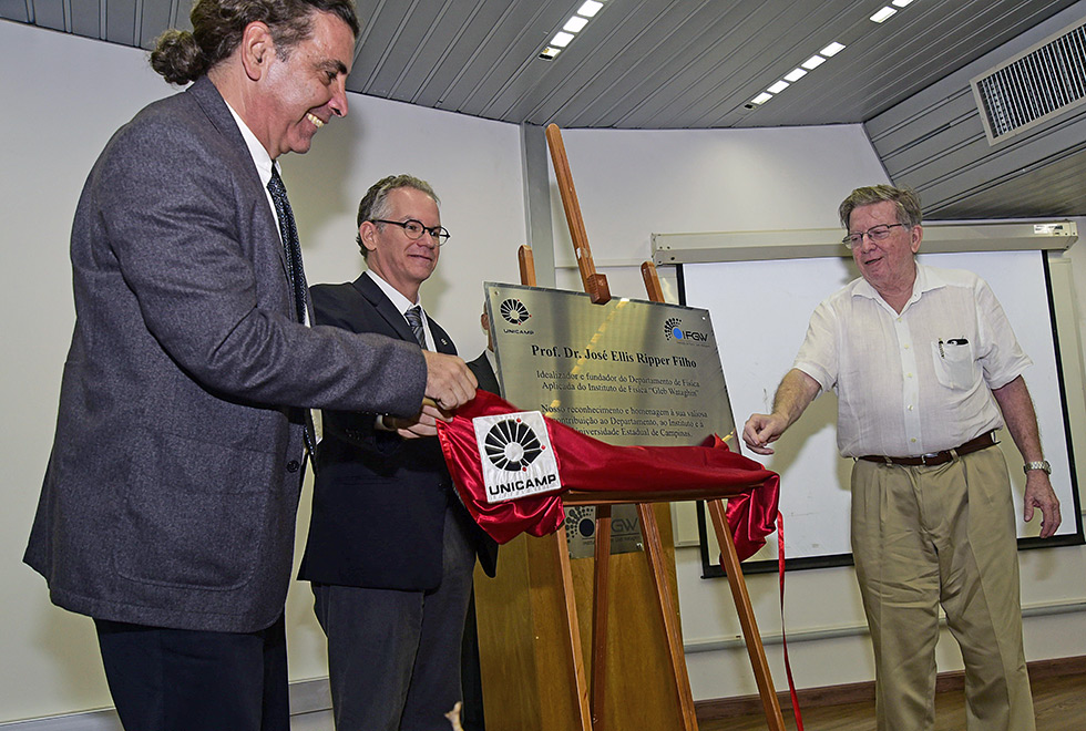 homens tiram pano vermelho de inauguração de placa de homenagem ao professor