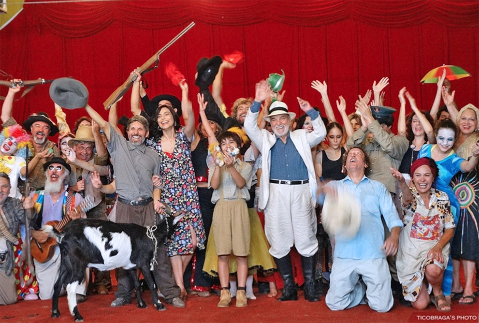 Toda a equipe do filme, inclusive o ator Lima Duarte, posam para a foto sorridentes, sobre um palco e com uma cabra