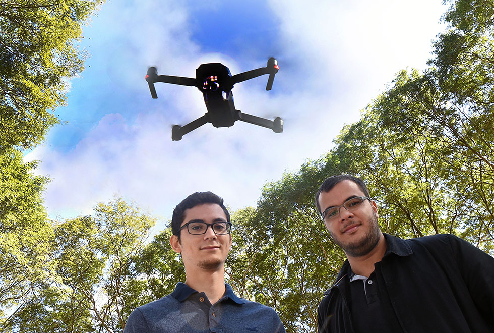 dois jovens em primeiro plano com drone voando ao fundo
