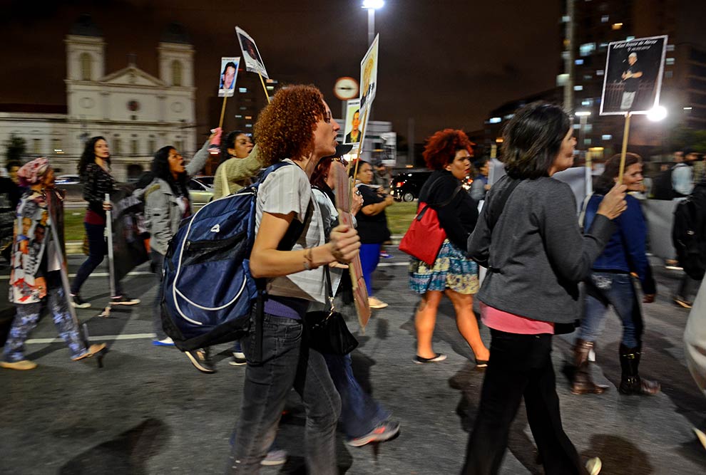 Foto mostra mulheres caminhando em uma manifestação na rua. Elas carregam cartazes.