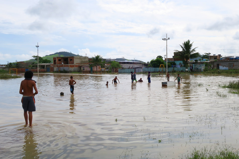 audiodescrição: fotografia colorida mostra área inundada. e crianças estão no meio da água