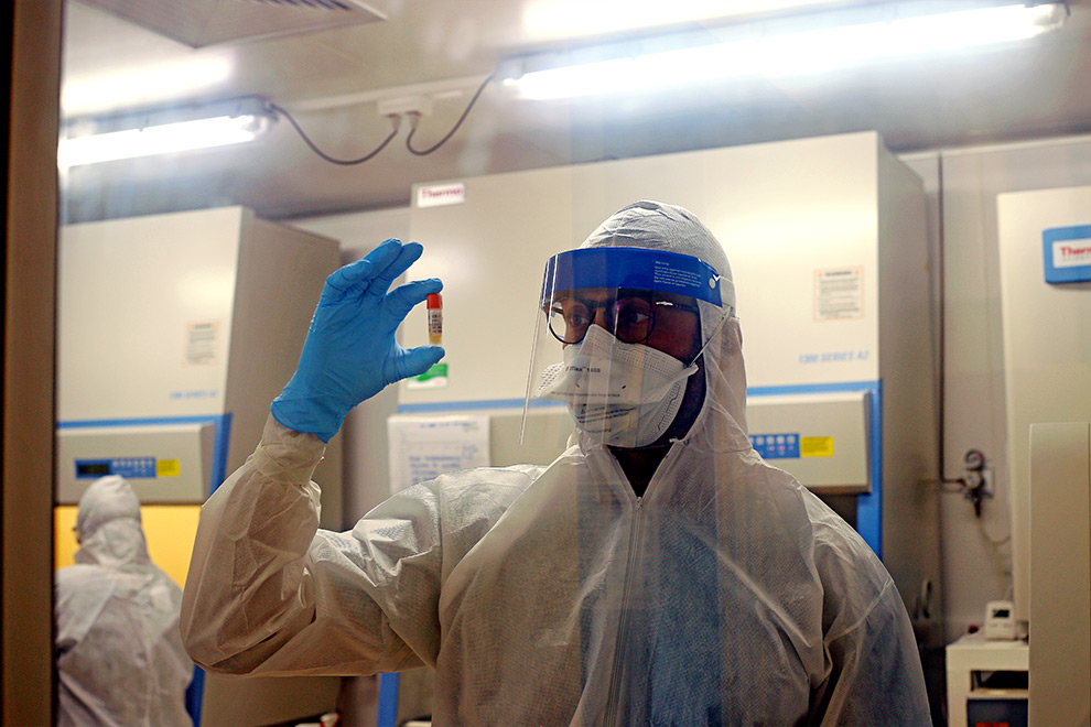 foto mostra pesquisador, com roupas e equipamentos de proteção, segurando uma amostra de coronavirus em um pequeno frasco