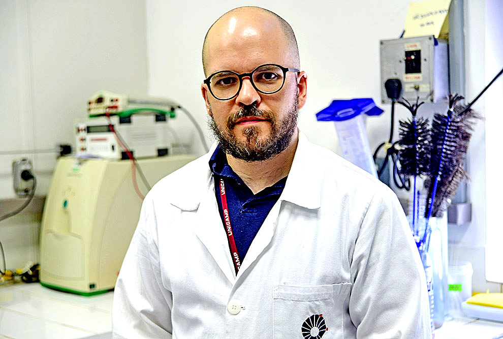foto mostra o professor marcelo mori. ele é careca, usa barba e óculos, veste jaleco branco e está em um laboratório