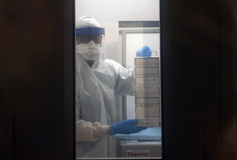 audiodescrição: fotografia colorida mostra pesquisador retirando o vírus Covid-19 do refrigerador