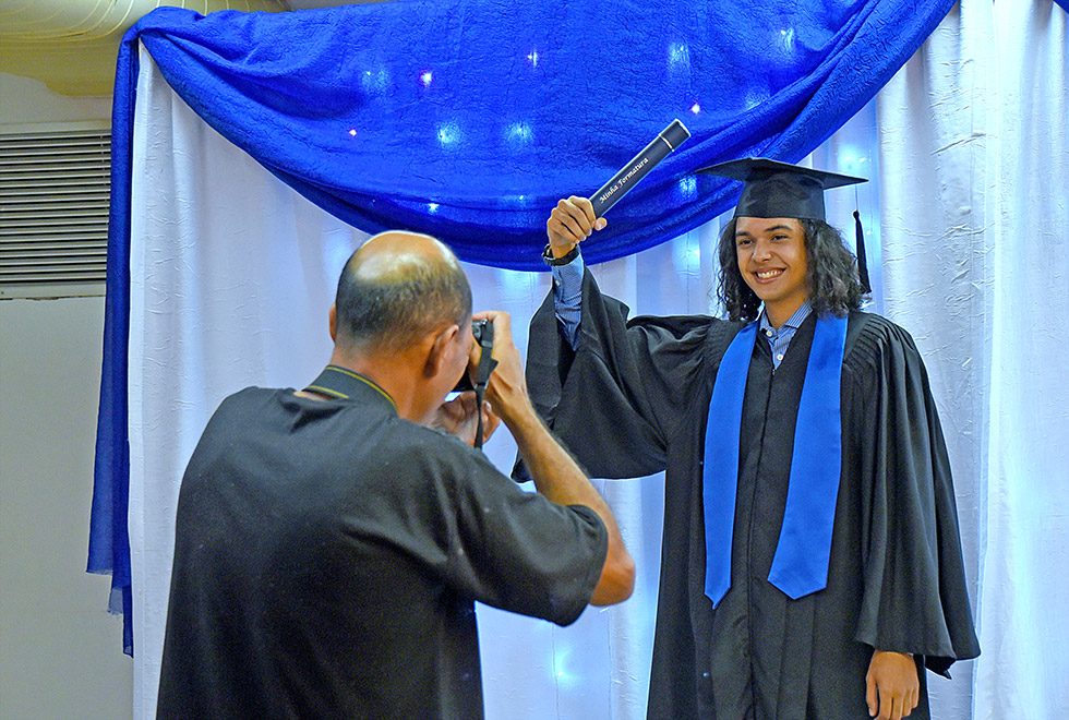 Marcos, de beca, levanta o canudo para foto do álbum de formatura