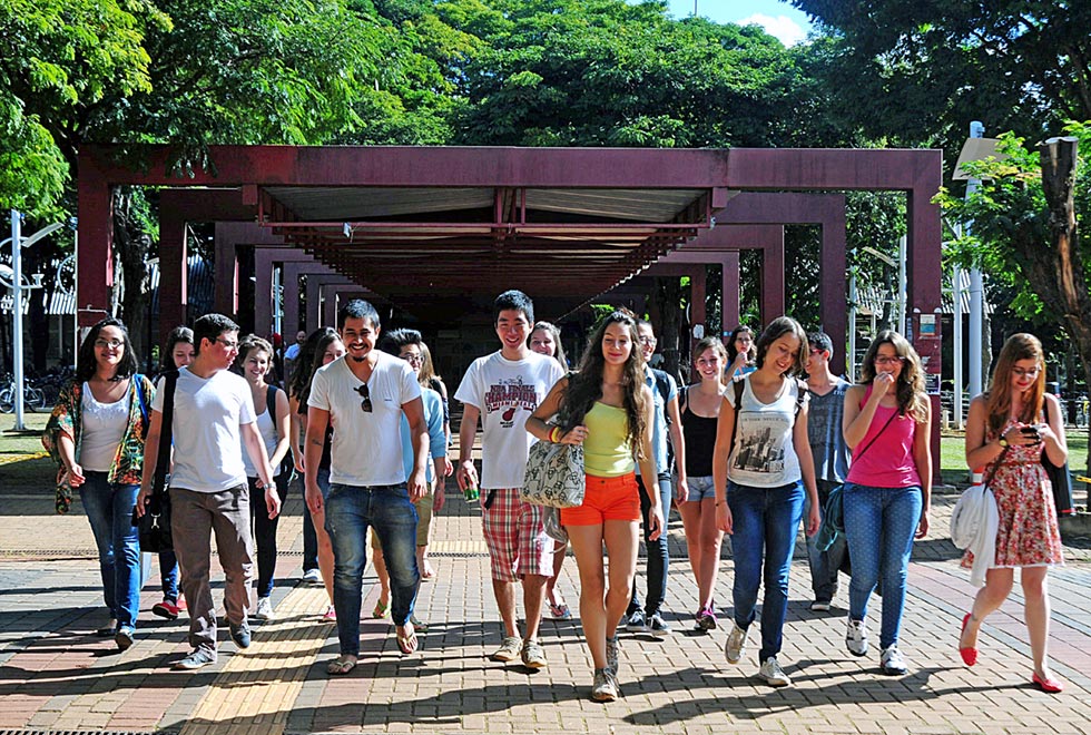 Estudantes caminham de frente para a cãmera em foto tirada próximo ao restaurante universitário. o grupo tem vários estudantes e todos se vestem de maneira despojada