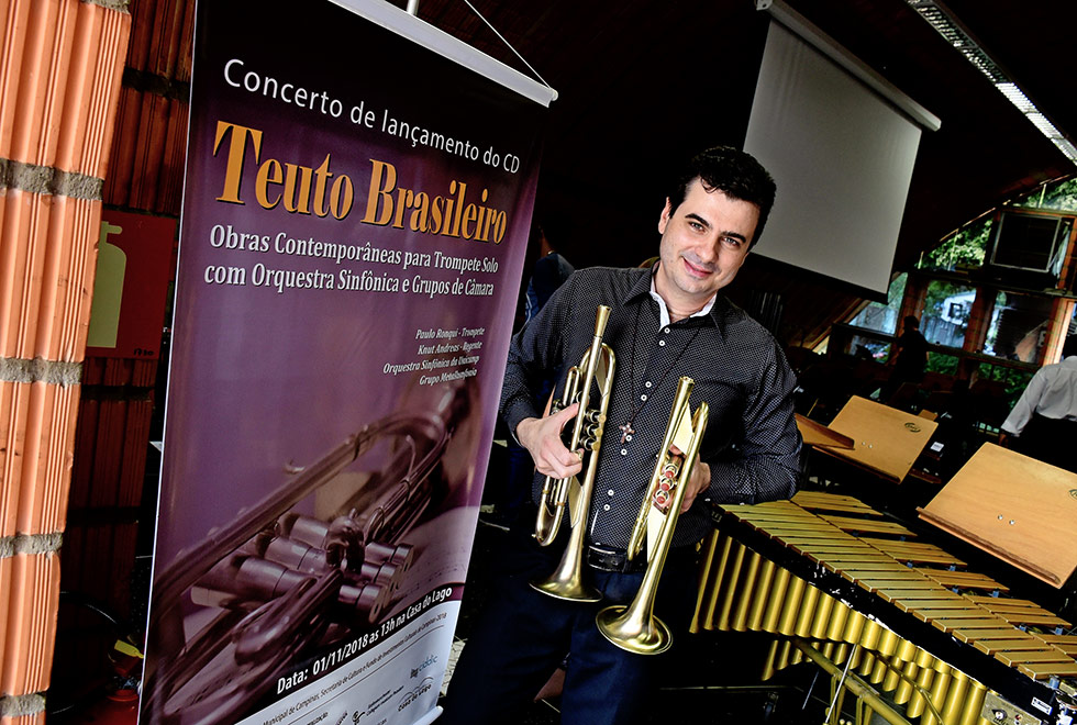 trompetista Paulo Ronqui está ao lado do cartaz com ilustração da capa do cd