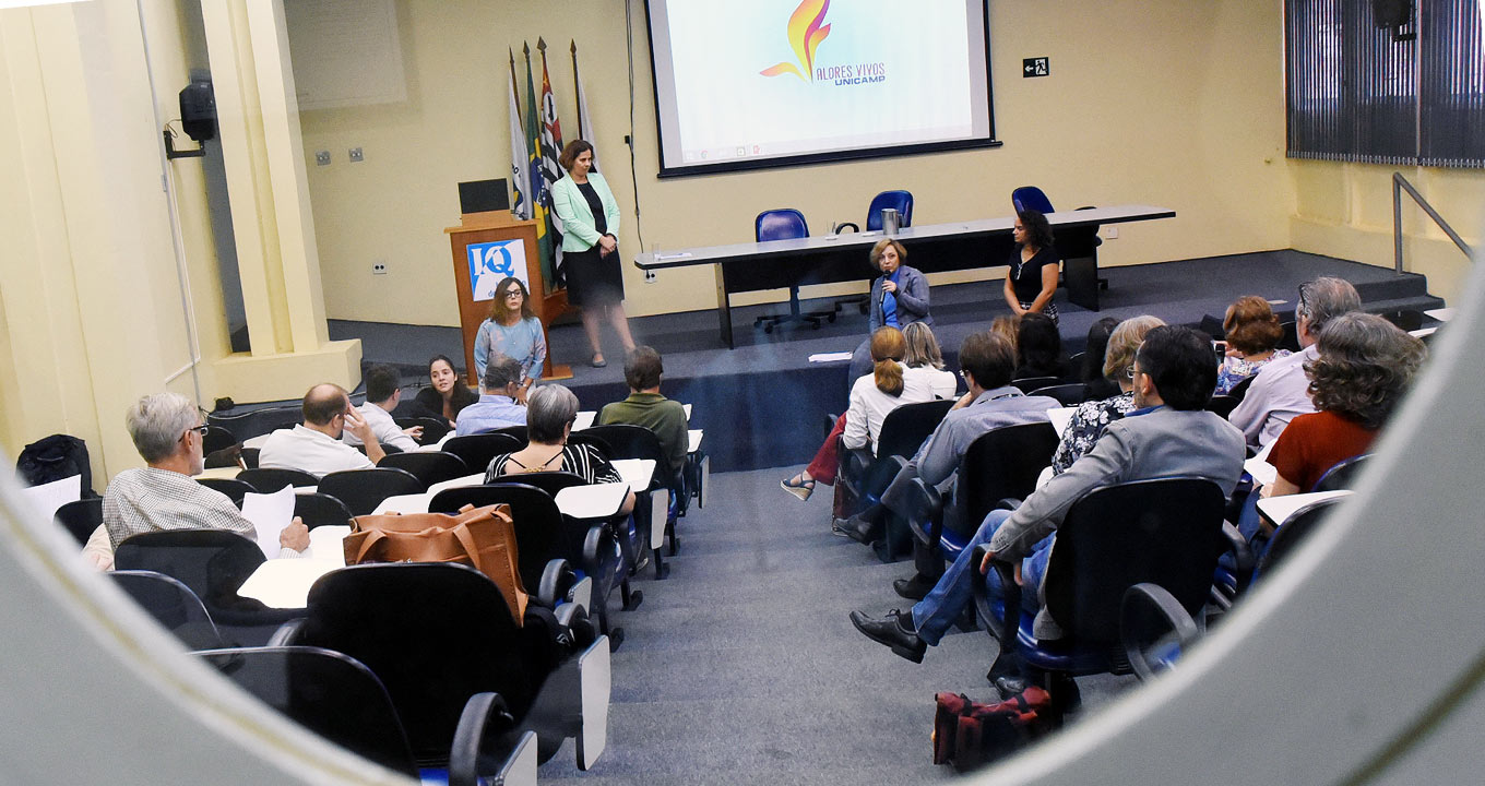 A professora Eliana Amaral, pró-reitora de Graduação, fala durante o workshop “Valores Vivos”, que ocorreu no dia 15 na Unicamp: envolvimento de membros da Administração Central e do Conselho Universitário | Foto: Antoninho Perri Em auditório, imagem panorâmica e frontal, quatro pessoas no palco de um auditório, sendo que à frente delas encontra-se o público do auditório, cerca de vinte pessoas, de costas na imagem, sentadas em cadeiras dispostas uma ao lado da outra, formando várias fileiras, e um corredor central. No palco, há duas pessoas à esquerda, uma sentada e outro em pé, e duas ao centro, sentadas, sendo que uma delas fala ao microfone. Ao fundo, há uma tela de projeção de data show, onde se lê Valores Vivos. Imagem 1 de 1.