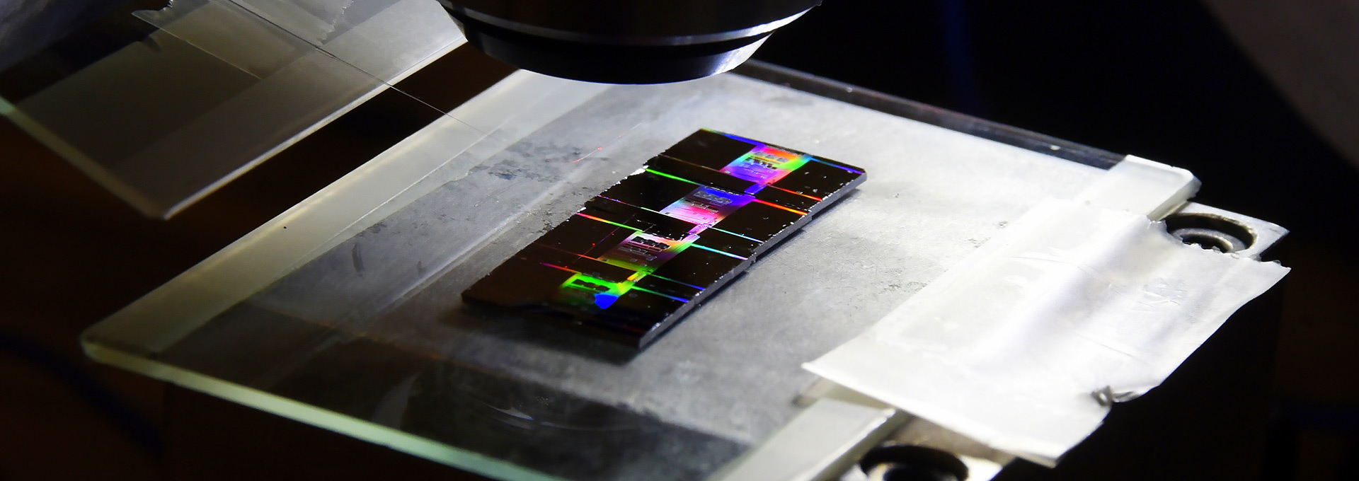 Luz conduzida por fibra óptica ilumina chips de silício, produzindo um efeito de arco-íris, sobre um fundo preto 