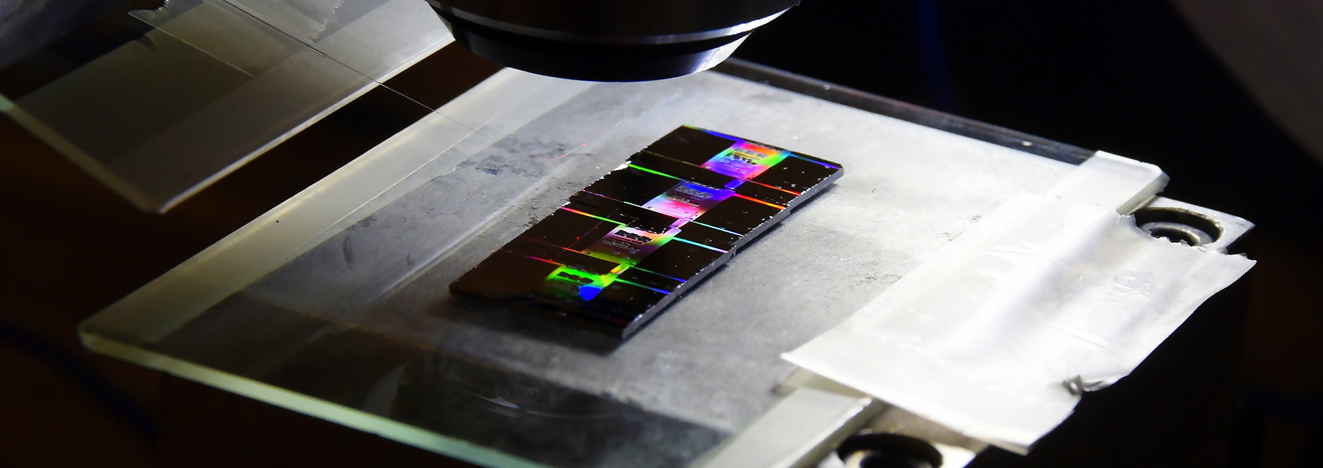 Chips de silício com milímetros de lado podem conter milhares de componentes Luz conduzida por fibra óptica ilumina chips de silício, produzindo um efeito de arco-íris, sobre um fundo preto
