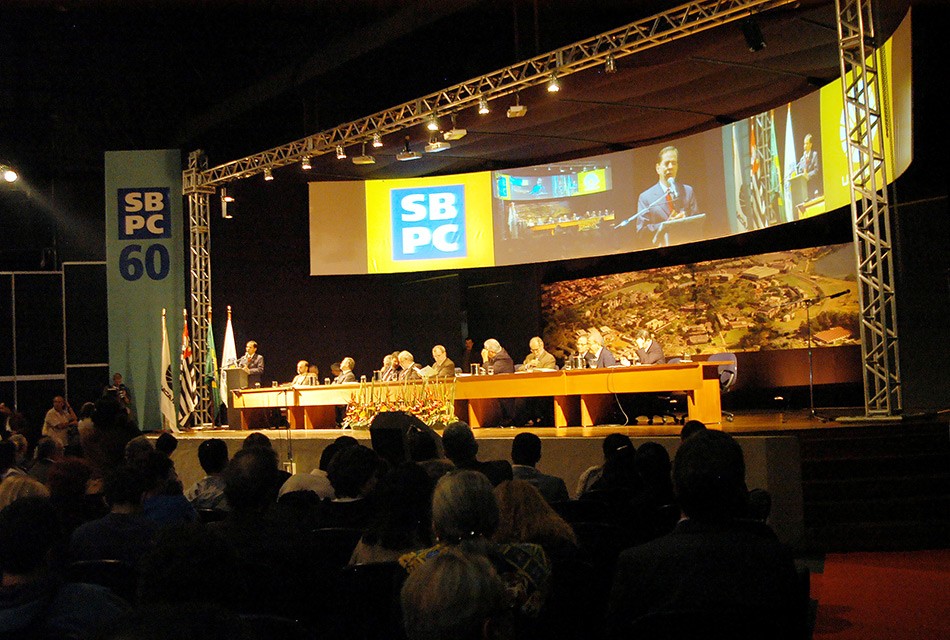 Abertura solene da reunião da Sociedade Brasileira para o Progresso da Ciência em 2008. À frente mesa com autoridades sentadas e atrás um telão iluminado onde passa um vídeo