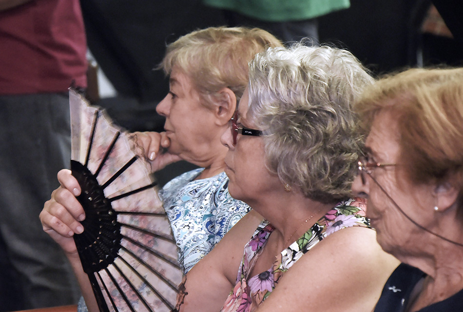 três senhoras idosas sentadas. A do meio se abana com  um leque.