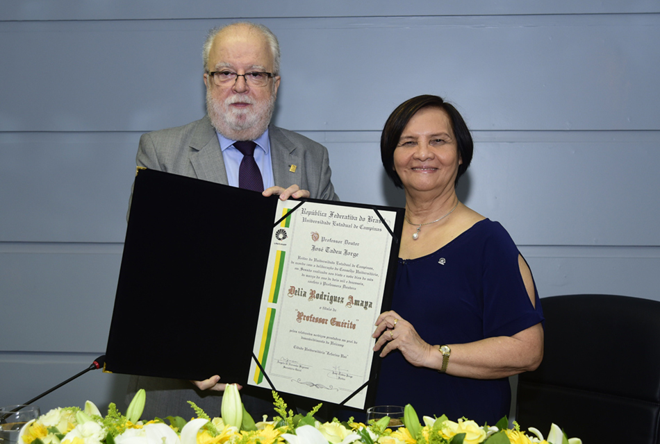 O reitor José Tadeu Jorge fez a entrega do título à professora José Tadeu Jorge e Delia posam para a foto junto ao título