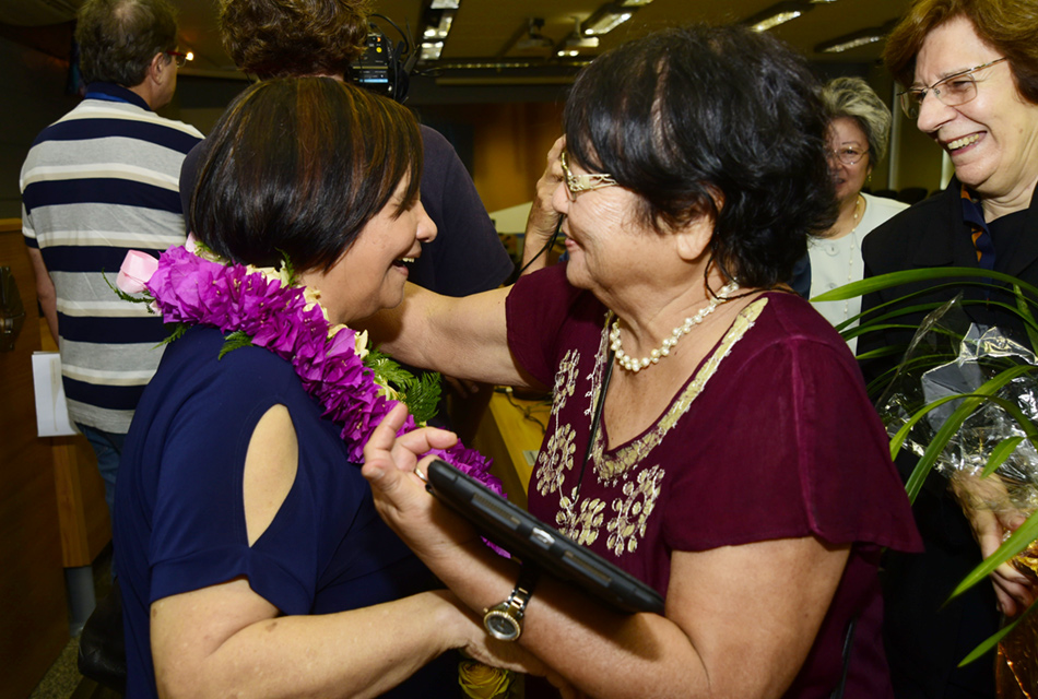 Presente: um colar de flores A professora recebe o abraço de uma amiga um colar de flores