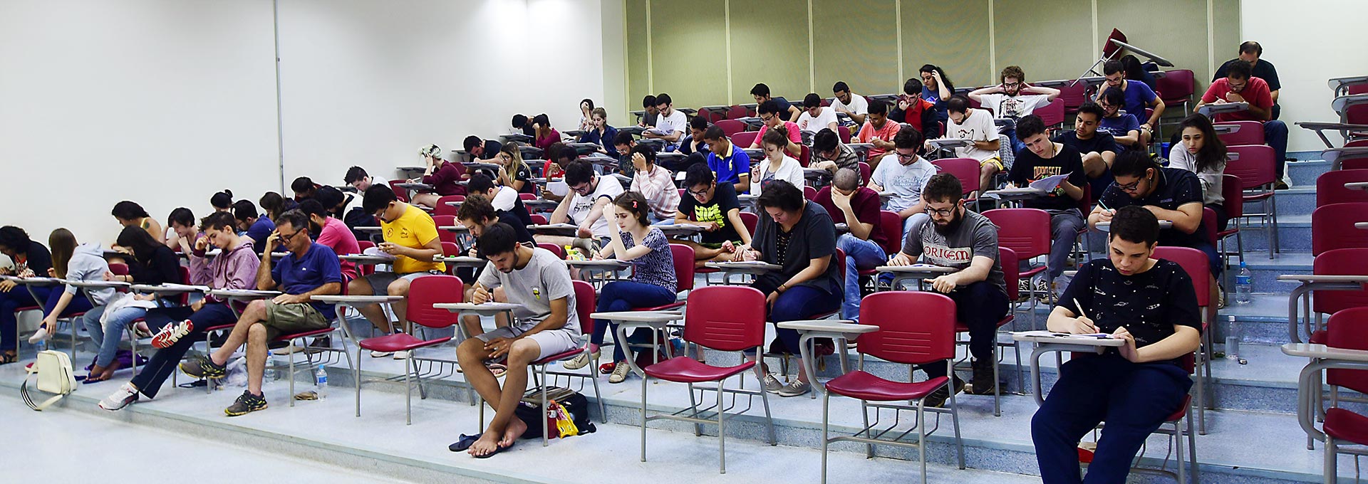 Sala de aula com cadeiras dispostas em fileiras, estudantes realizando as provas, algumas caeiras vazias.