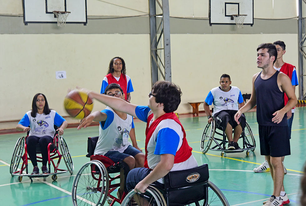 Estudantes sobre as cadeiras de roda simulam um jogo de basquete adaptado