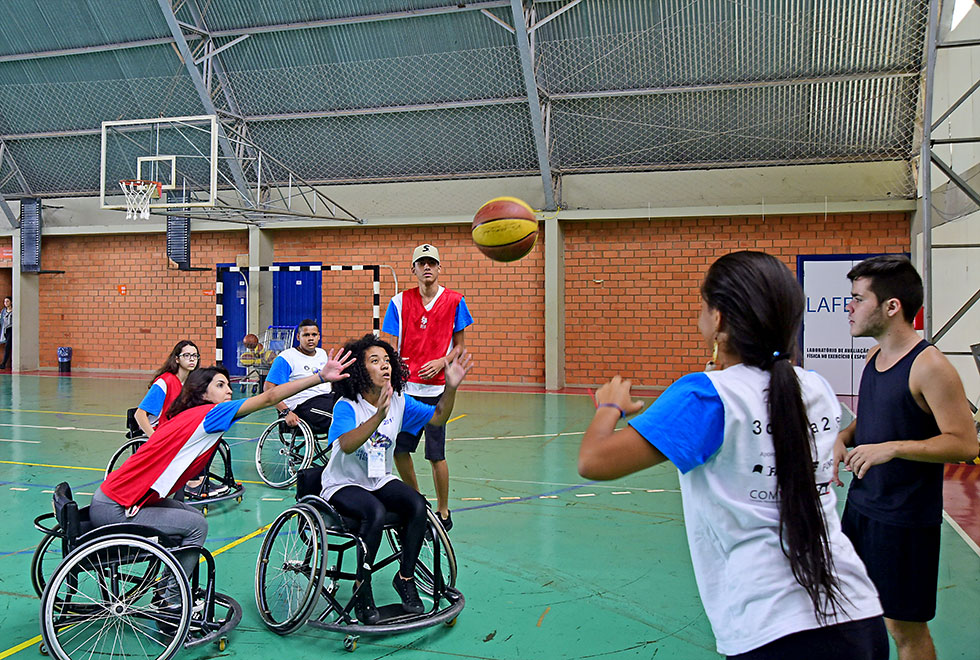 Estudantes sobre as cadeiras de roda simulam um jogo de basquete adaptado