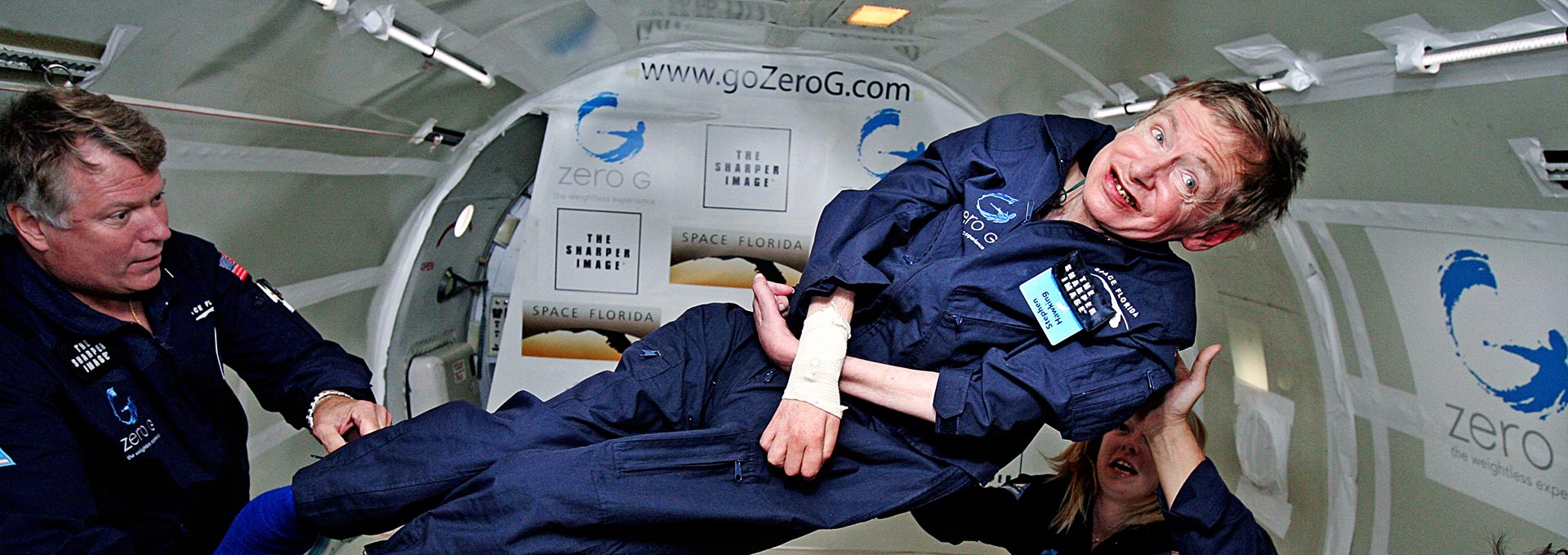 Em experiência na Nasa, Stephen Hawking realiza um sonho aos 65 anos: flutuar Audiodescrição: Em cabine metálica em formato tubular semelhante à parte interna de um avião, homem flutua com os braços cruzados em xis, na altura da barriga, sendo que ele está na horizontal, com a cabeça para a direita na imagem. Ele veste um macacão azul. Ao fundo, há uma placa afixada onde se lê www.gozerog.com. Há um homem à esquerda que dá apoio às pernas do homem que flutua, e duas pessoas à direita que sustentam suas costas. A cabine é revestida com material para proteção de impactos. Imagem 1 de 1