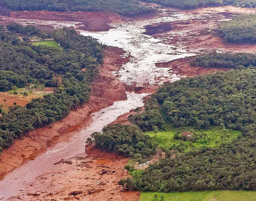 Região atingida pelo rompimento da barragem Mina Córrego do Feijão, em Brumadinho/MG. Publicado em 26/01/2019 - 12:07 | Foto: Agência Brasil - Divulgação Audiodescrição:Em imagem panorâmica, foto aérea de amplas áreas com vegetação à esquerda e à direita, sendo que ao centro há um rio repleto de lama que cruza a imagem, vindo de cima para baixo. Há uma grande área com lama e barro na parte de cima de imagem.