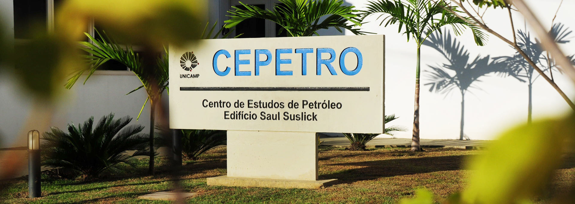 Faixada do Cepetro onde será instalada novo laboratório de pesquisas relacionadas ao petróleo Audiodescrição: Em área externa, imagem frontal de placa de concreto com cerca de um metro de altura, dois de largura e vinte centímetros de profundidade, onde se lê em letras azuis em baixo relevo Cepetro, em destaque, com logo da Unicamp à esquerda na imagem. A placa está afixada em uma base de concreto, sendo que no entorno dela há uma área ajardinada, com pedriscos e plantas ornamentais como bromélias e palmeiras. Ao fundo, paredes brancas de edificação em alvenaria. A área é ensolarada. Imagem 1 de 1.