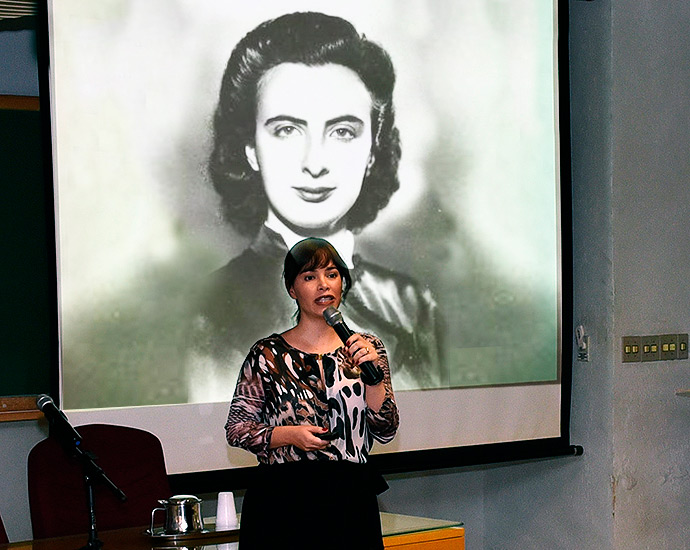 Palestrante Thaissa Proni. Ao fundo montagem com a foto de Elza Gomide Montagem mostra palestrante do grupo Elza com foto de Elza Gomide ao fundo