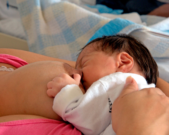 Imagem de um bebê recém-nascido dormindo abraçado ao seio da mãe 