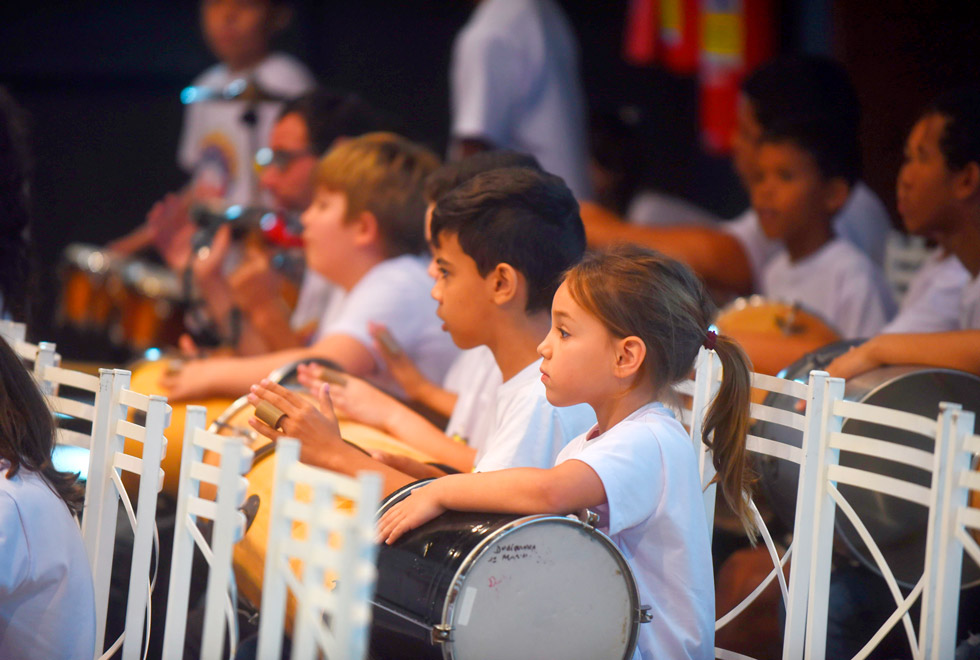 Recorte de uma cena das crianças que cantaram no coral e seus instrumentos de percussão