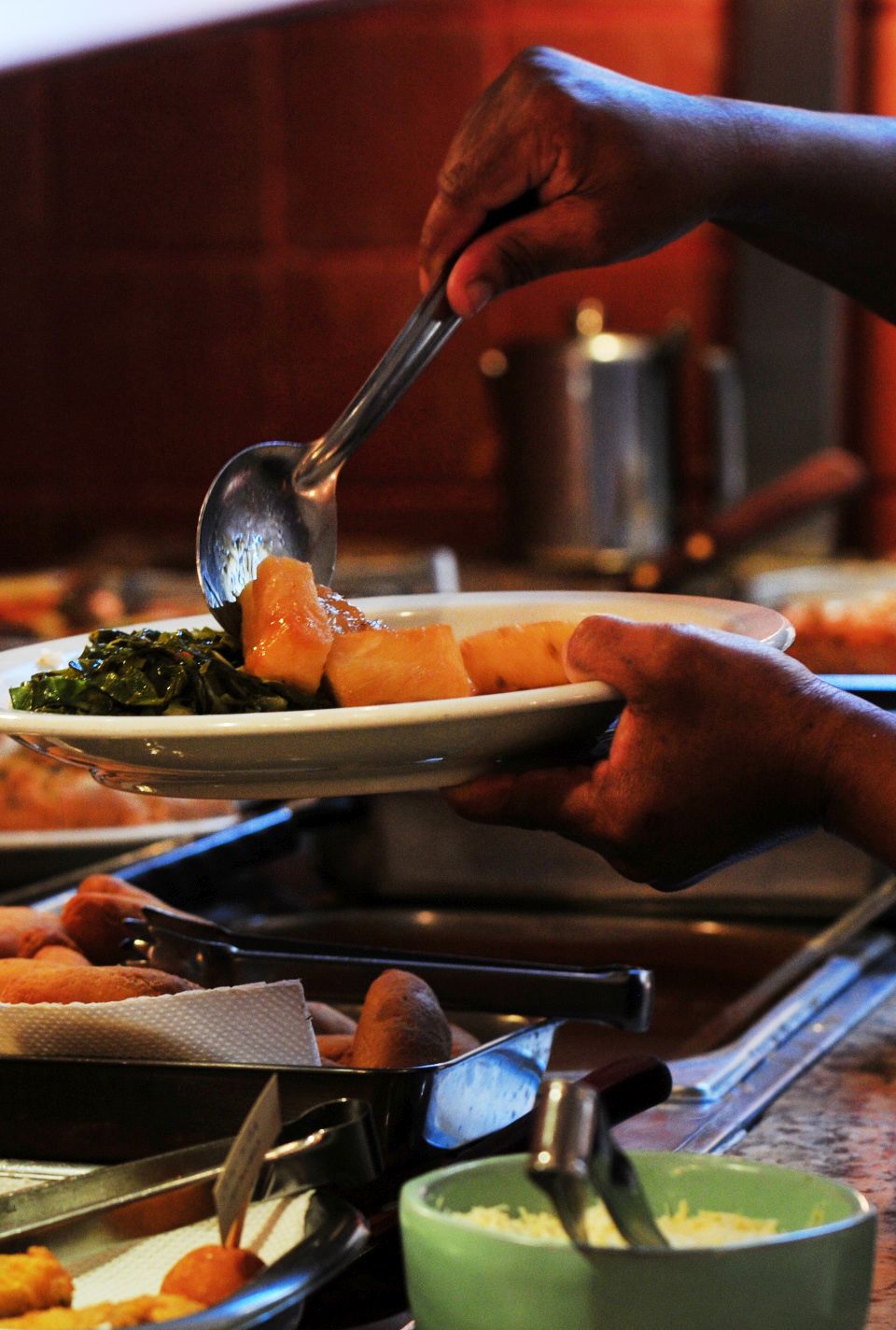 Foto tirada em restaurante mostra uma pessoa se servindo com detalhe nas mãos e no prato