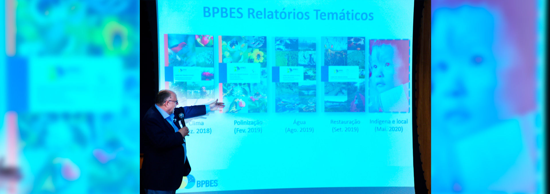 ‘Biodiversidade não é problema, é solução’, evento realizado nesta segunda-feira no Centro de Convenções Audiodescrição: no palco de um auditório, imagem em perfil e em plano médio, homem em pé à esquerda na imagem e com olhar voltado para a direita, fala em microfone sem fio segurando-o com a mão direita, enquanto que com o braço esquerdo aponta para uma ampla tela de data show que exibe o título BPBES Relatórios Temáticos e, abaixo, cinco capas de livros compostas por fotos e com títulos como clima, polinização, água e indígenas. O homem usa óculos e veste blazer preto. Imagem 1 de 1.