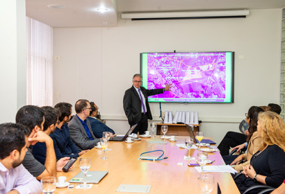Marcelo Knobel apresentou o projeto do HIDS Reitor aparece em pé ao fundo ao lado de um telão, falando para os membros da reunião