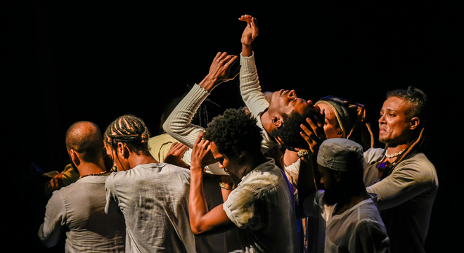 Espetáculo Negra Palavra integra a programação. Foto: Mariana Prieto audiodescrição: fotografia colorida. seis homens negros levantam um outro homem, que está deitado e com as mãos para cima. a expressão nos rostos deles é de tristeza.