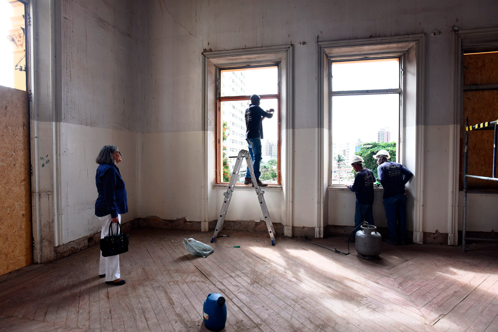 audiodescrição: fotografia colorida mostra trabalhadores com capacetes trabalhando em janelas. a coordanadora geral da unicamp, teresa atvars, está olhando o trabalho