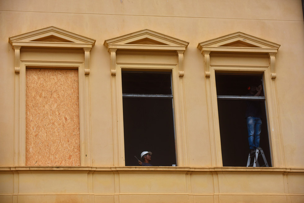 audiodescrição: fotografia colorida mostra fachada de prédio amarelo, um casarão histórico. há dois homens na janela trabalhando em revitalização