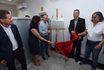 Descerramento da placa do novo prédio da Deas Audiodescrição fotografia colorida mostra o reitor da Unicamp, Marcelo Knobel, a coordenadora geral da Unicamp, teresa Atvars, o diretor executivo da área de saúde, Manoel Bertolo, Sueli Rangel, assessora da diretoria e o diretor da Faculdade de Ciências Médicas, Luiz Carlos Zeferino, em frente à placa de inauguração da diretoria executiva da área de saúde. Na foto, o reitor e Sueli estão com um tecido vermelho nas mãos, descobrindo a placa.