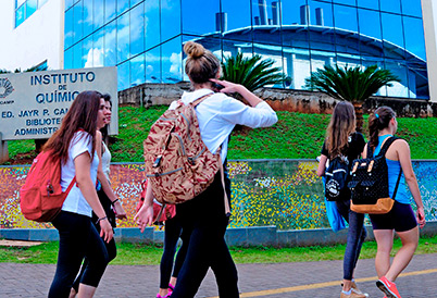 audiodescrição: fotografia colorida mostra prédio do instituto de química. estudantes estão caminhando em frente ao prédio.