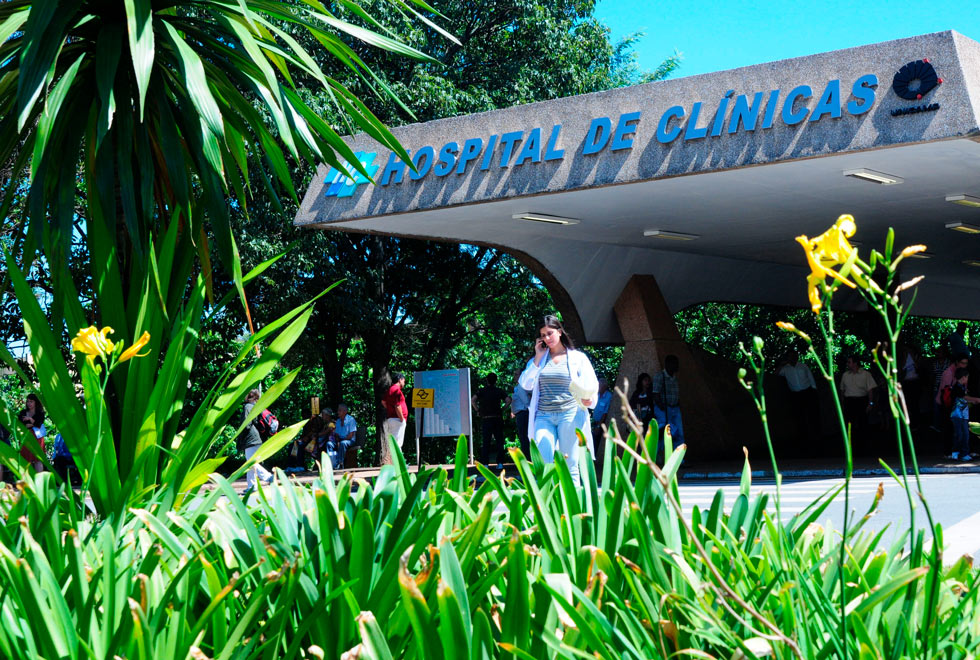 foto mostra a entrada do hospital de clínicas da unicamp com uma mulher, vestida com jaleco branco, saindo por ela