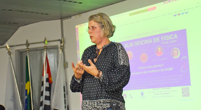 Física para Curiosos abre programação 2020 com diálogo sobre interdisciplinaridade foto mostra monica cotta, enquadrada da cintura para cima, no palco, durante sua apresentação. Clique enter para acessar
