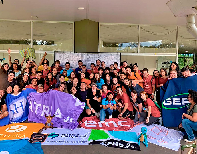 Turma de estudantes posam com bandeiras e camisetas das empresas juniores