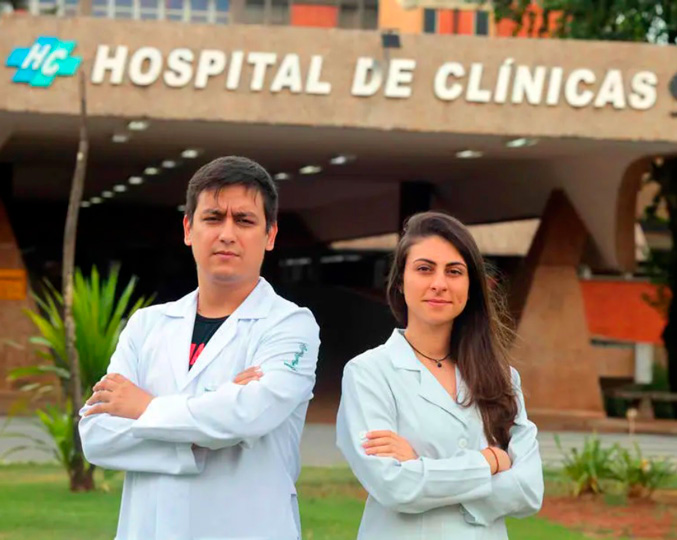 Zeus Tristão e Isabela Schoenacker se apresentaram coo voluntários para fazer a triagem de pacientes com sintomas da covid-19 Um homem e uma mulher com jalecos brancos em frente à rampa de entrada do HC