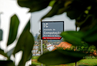 foto mostra uma placa indicando a localização do instituto de computação, ela é vista ao fundo por entre folhagens